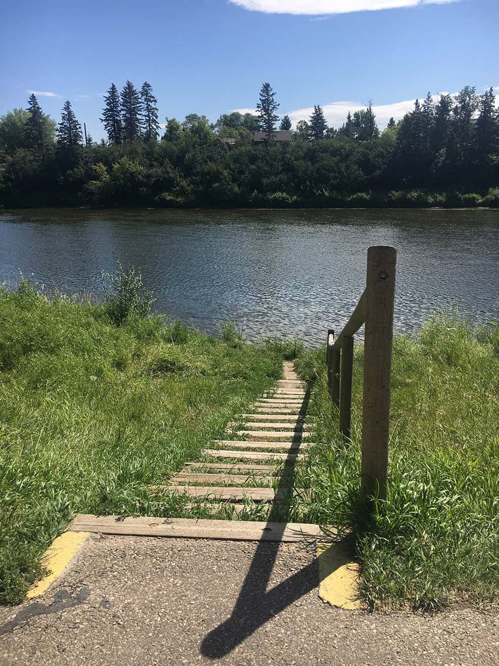 Path with stairs going down to the Red Deer river surrounded by green grass with a railing.