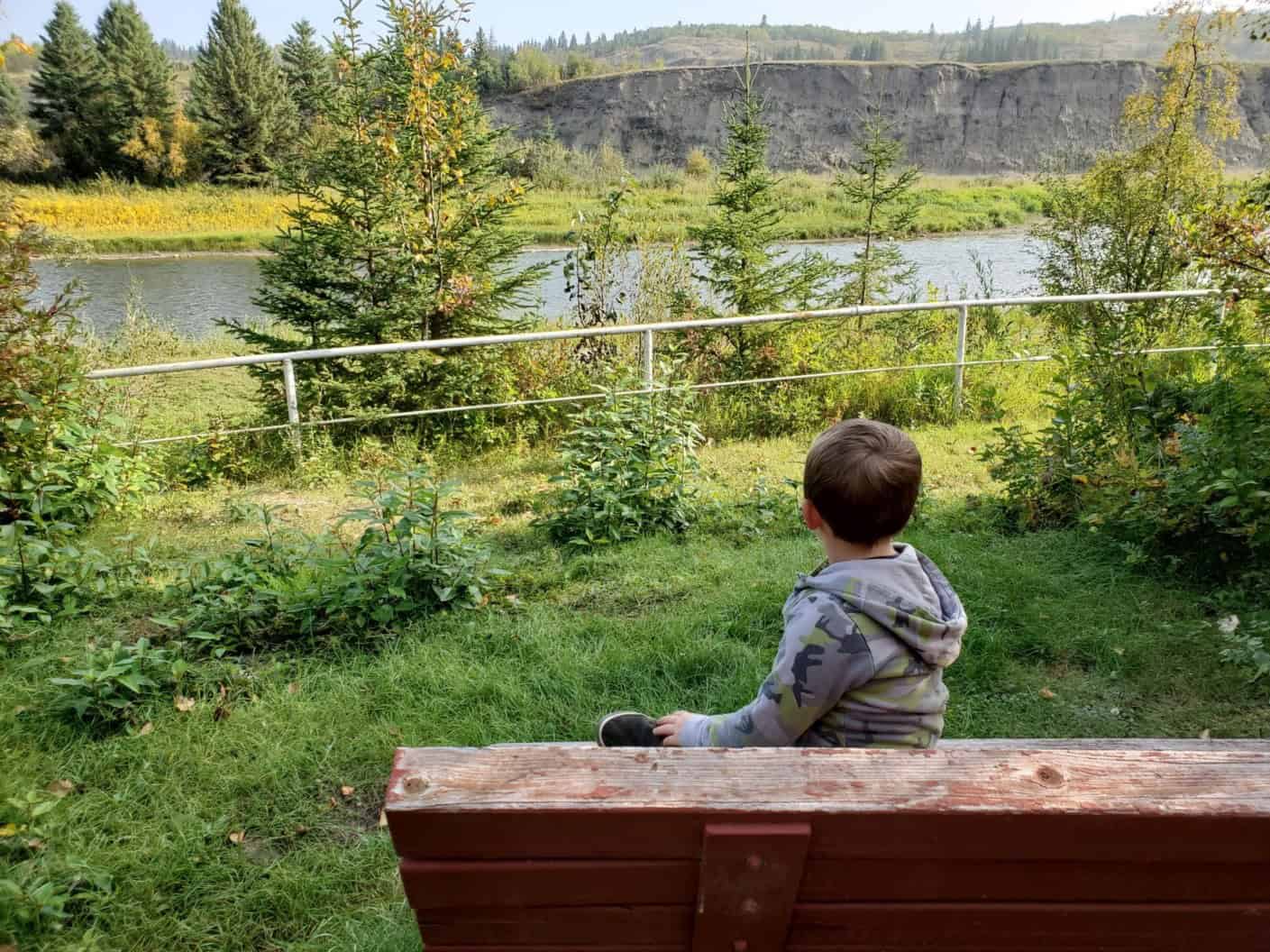 A child sitting on a bench at Trenville Park looking out to the river