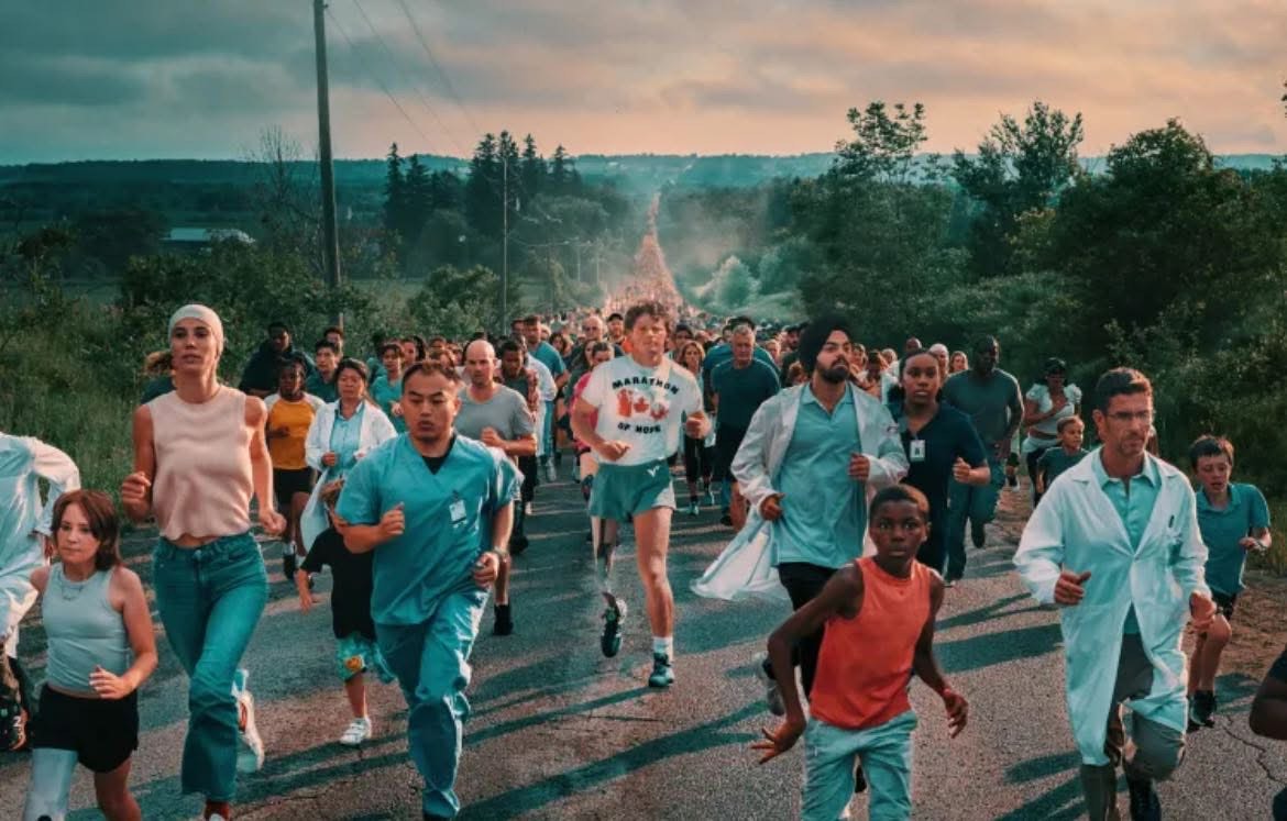 Runners participating in a community race on a rural road surrounded by green trees during sunset.